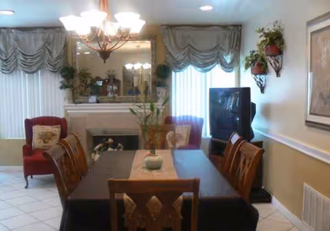 Dining room in a senior facility featuring a long table, chandelier, fireplace, and upholstered chairs.