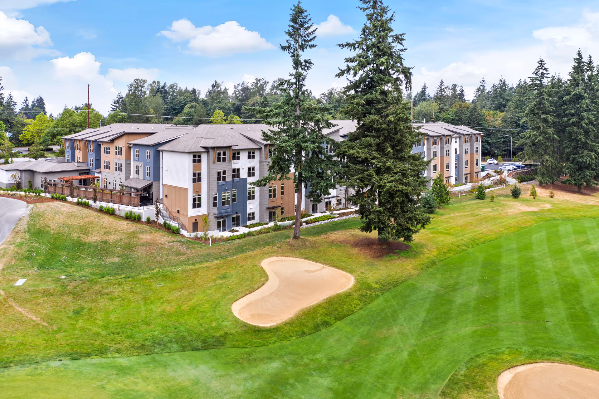 A multi-story senior living building set beside a green golf course with sand bunkers and tall trees.
