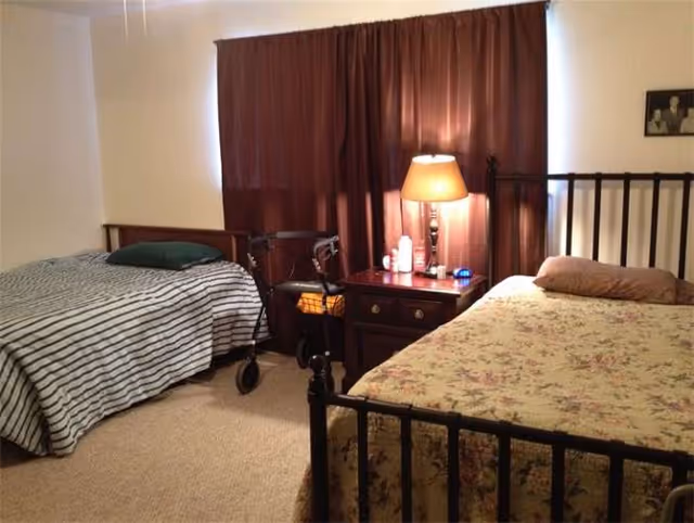 Two metal-framed beds with a nightstand, lamp, and a walker between them in a bedroom.