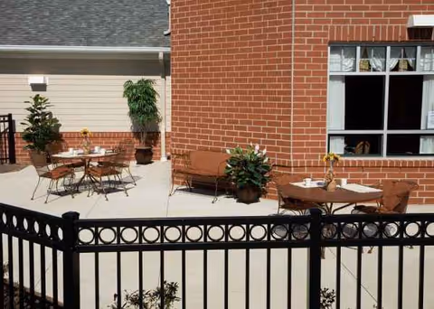 Outdoor patio with tables, chairs, and potted plants beside a brick building.