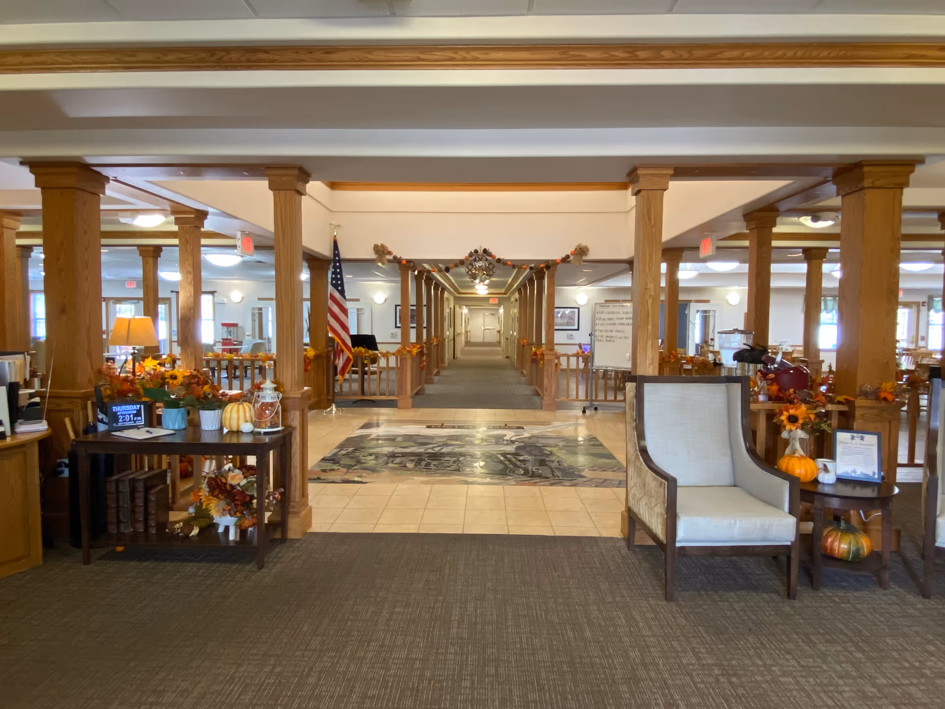 Spacious decorated lobby and common area with wooden columns, seating, an American flag, and a long central hallway.