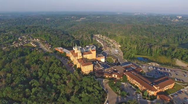 Aerial view of a large senior living campus with multiple connected buildings, parking areas, and surrounding wooded landscape.