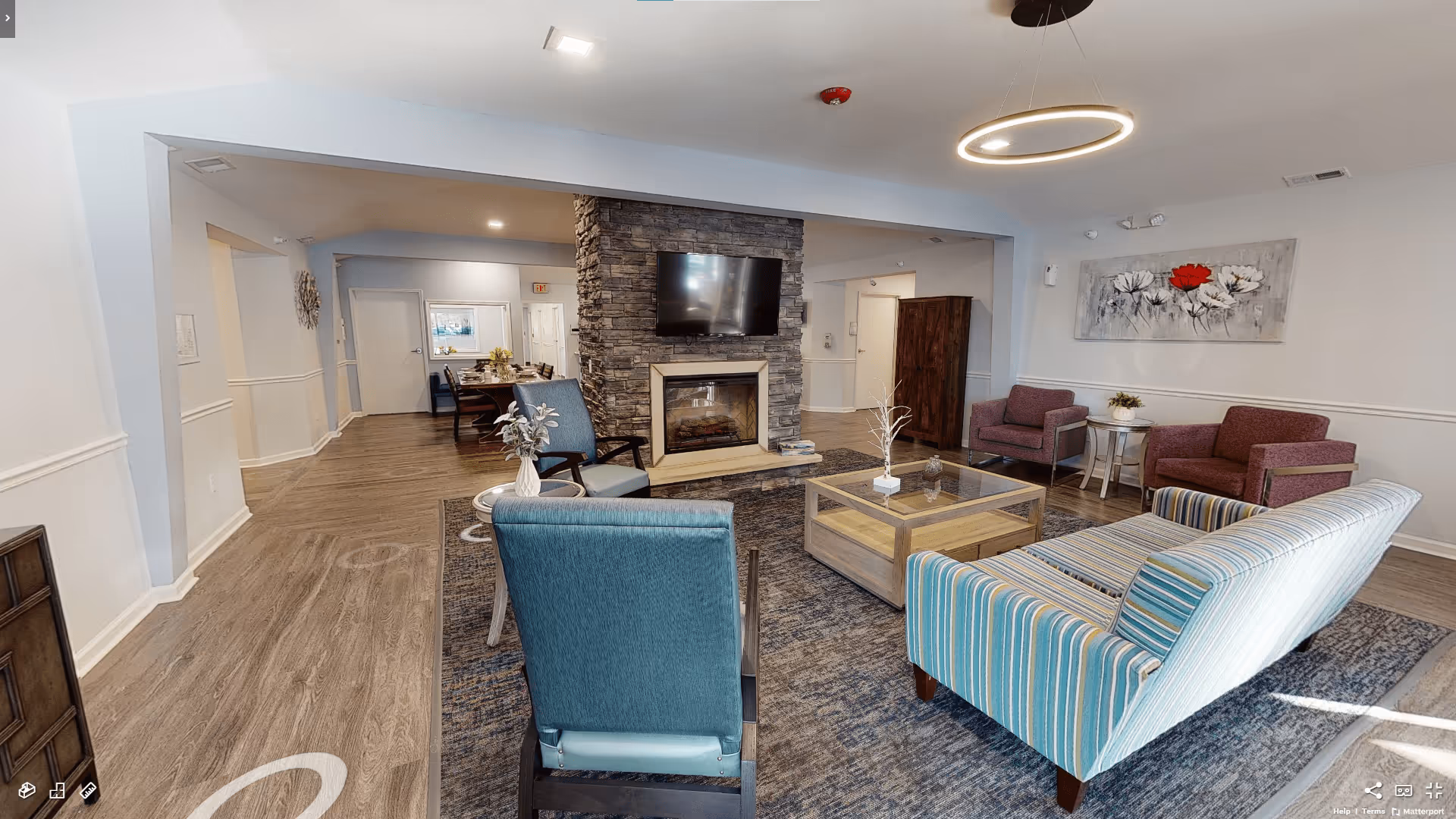 Communal living room with sofas and armchairs arranged around a coffee table and a stone fireplace with a mounted TV.