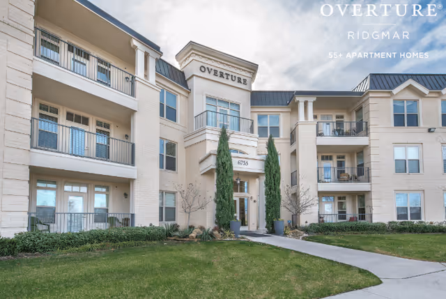 Front exterior of a three-story apartment-style senior living building with balconies, landscaping, and 'Overture' signage.