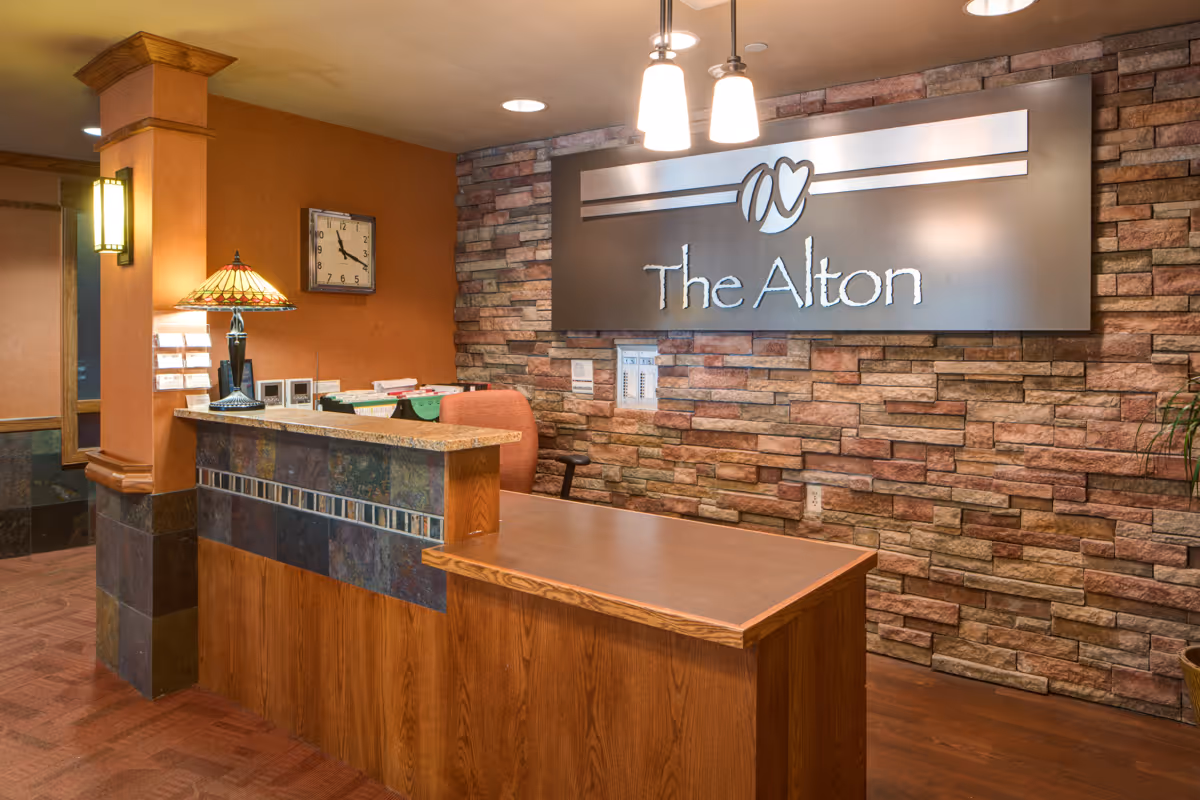 Warmly lit lobby reception desk with a stone accent wall and a sign reading "The Alton".