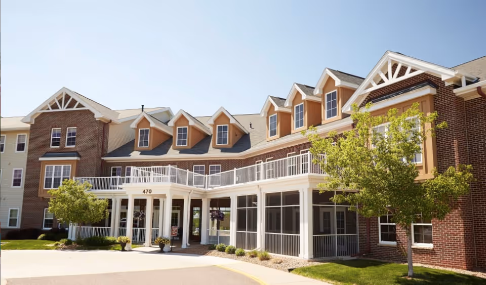 Front entrance of a brick senior living building with white columns, upper balconies and dormer windows.