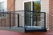 Exterior balcony with a black metal railing outside a sliding glass door on a brick-and-siding building.