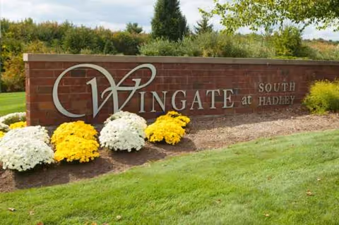Brick sign reading Wingate at South Hadley with yellow and white flowers.