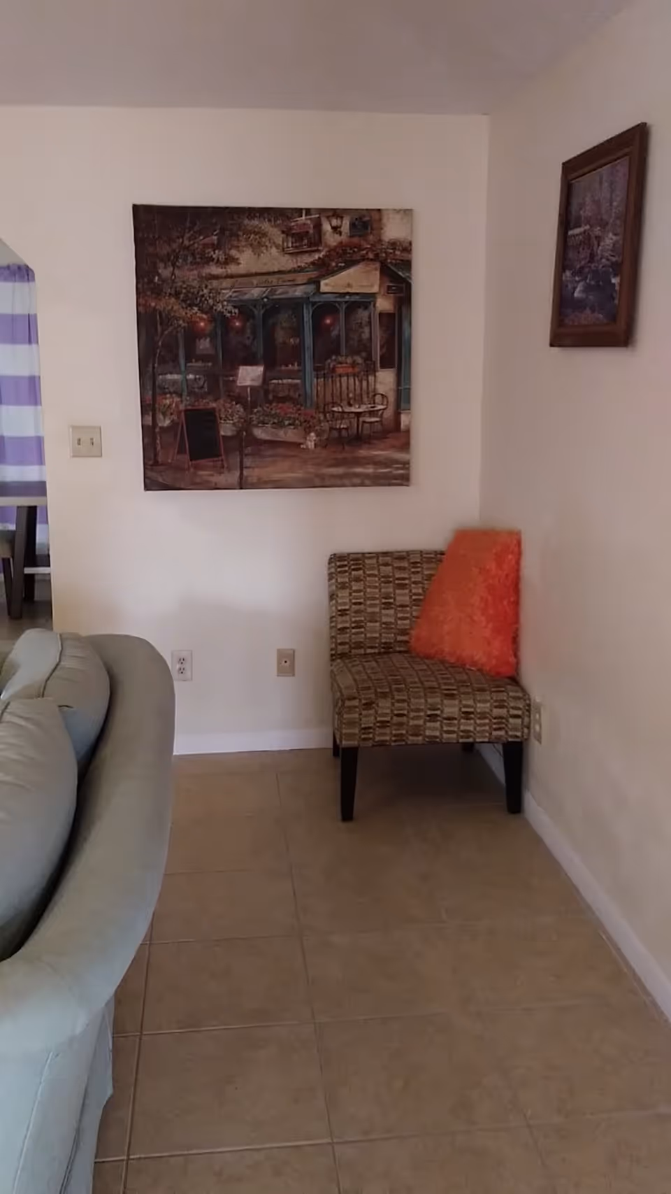 Corner of a senior living facility living room with a patterned chair, sofa, and wall art.