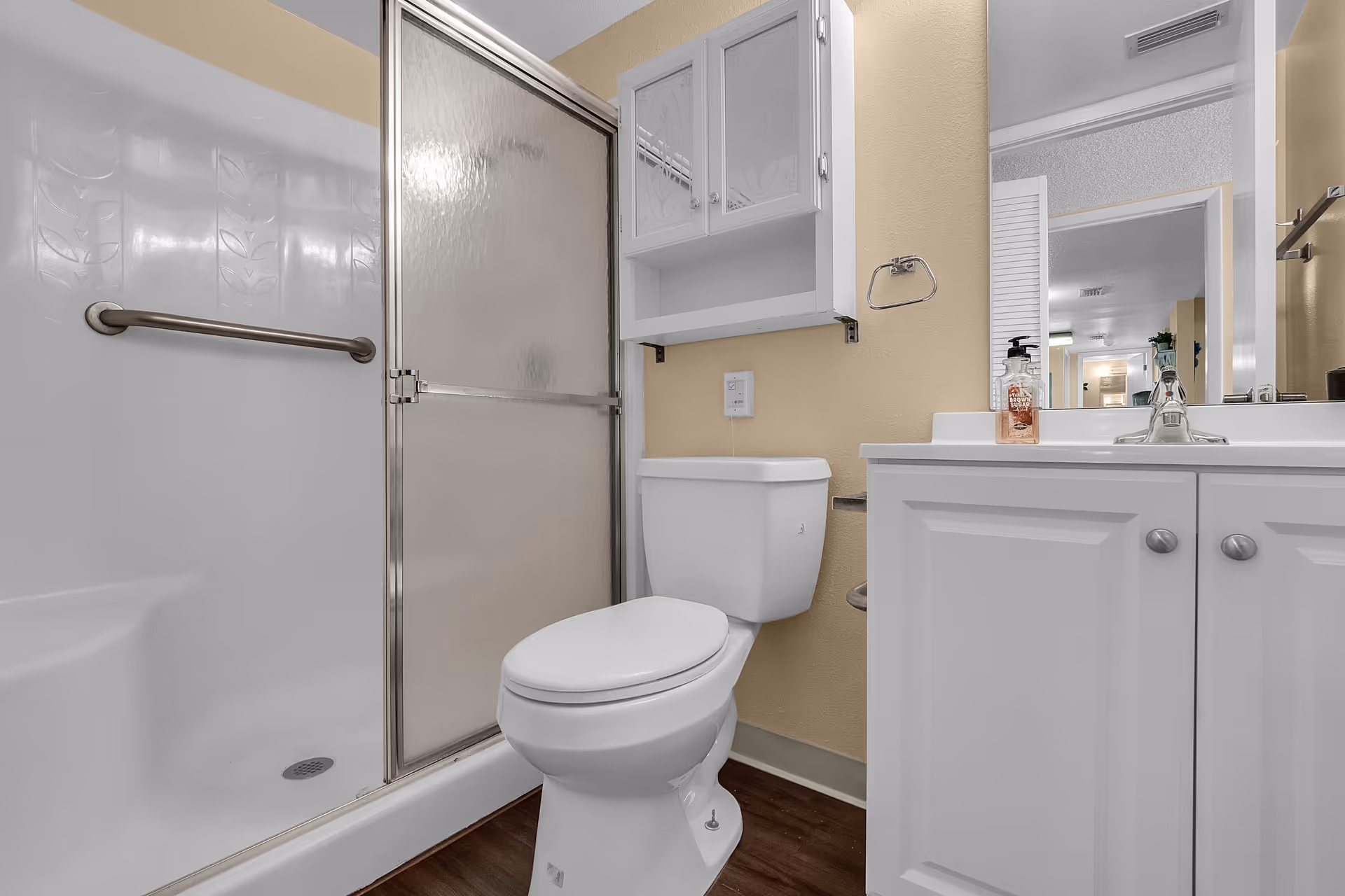 A clean bathroom with a shower stall with frosted sliding doors, a toilet, white vanity with sink and mirror, and a wall cabinet.