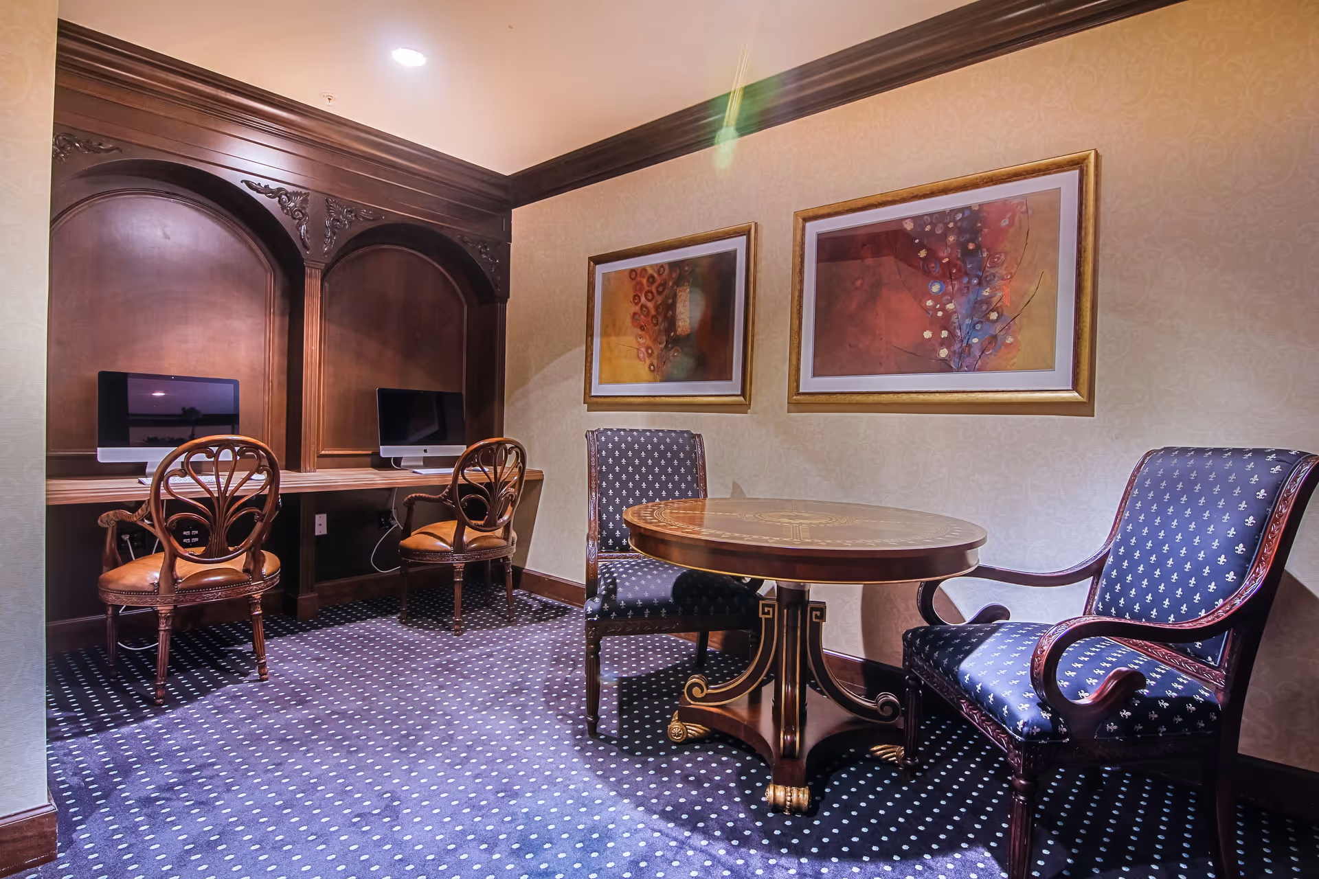 Well-appointed sitting area with a round wooden table, upholstered chairs, and two computer workstations set into carved wooden alcoves.