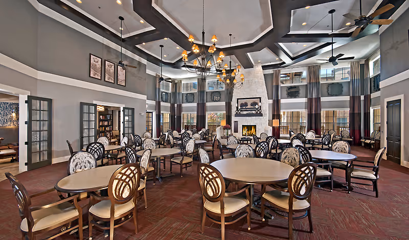 Spacious two-story dining room with round tables, upholstered chairs, a central chandelier, and a fireplace.