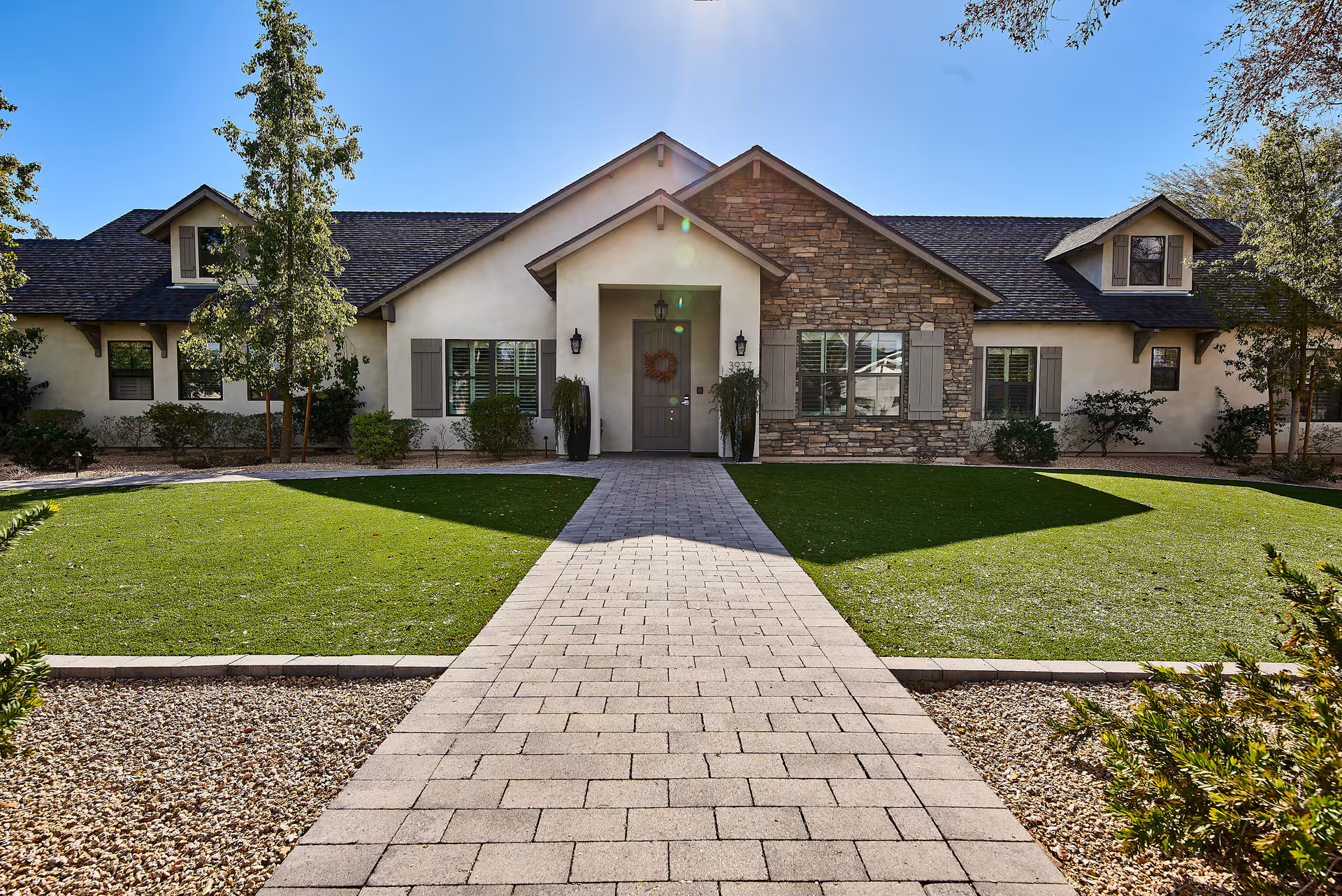 Front exterior of a single-story residential-style building with stone accents, a central doorway, paved walkway, and manicured lawn.
