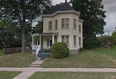 A two-story cream-colored house-style senior living facility with a front porch and green lawn.