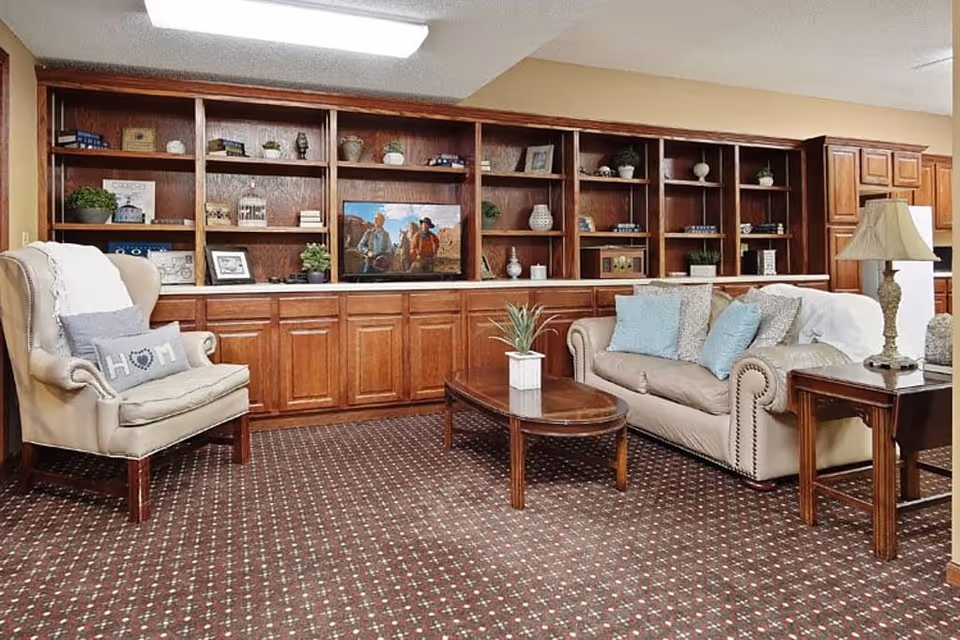 A cozy sitting area with an armchair, sofa, coffee table and built-in wooden shelving and cabinets along the back wall.