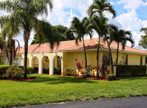 Yellow single-story building with arched entryway and palm trees around a manicured lawn.