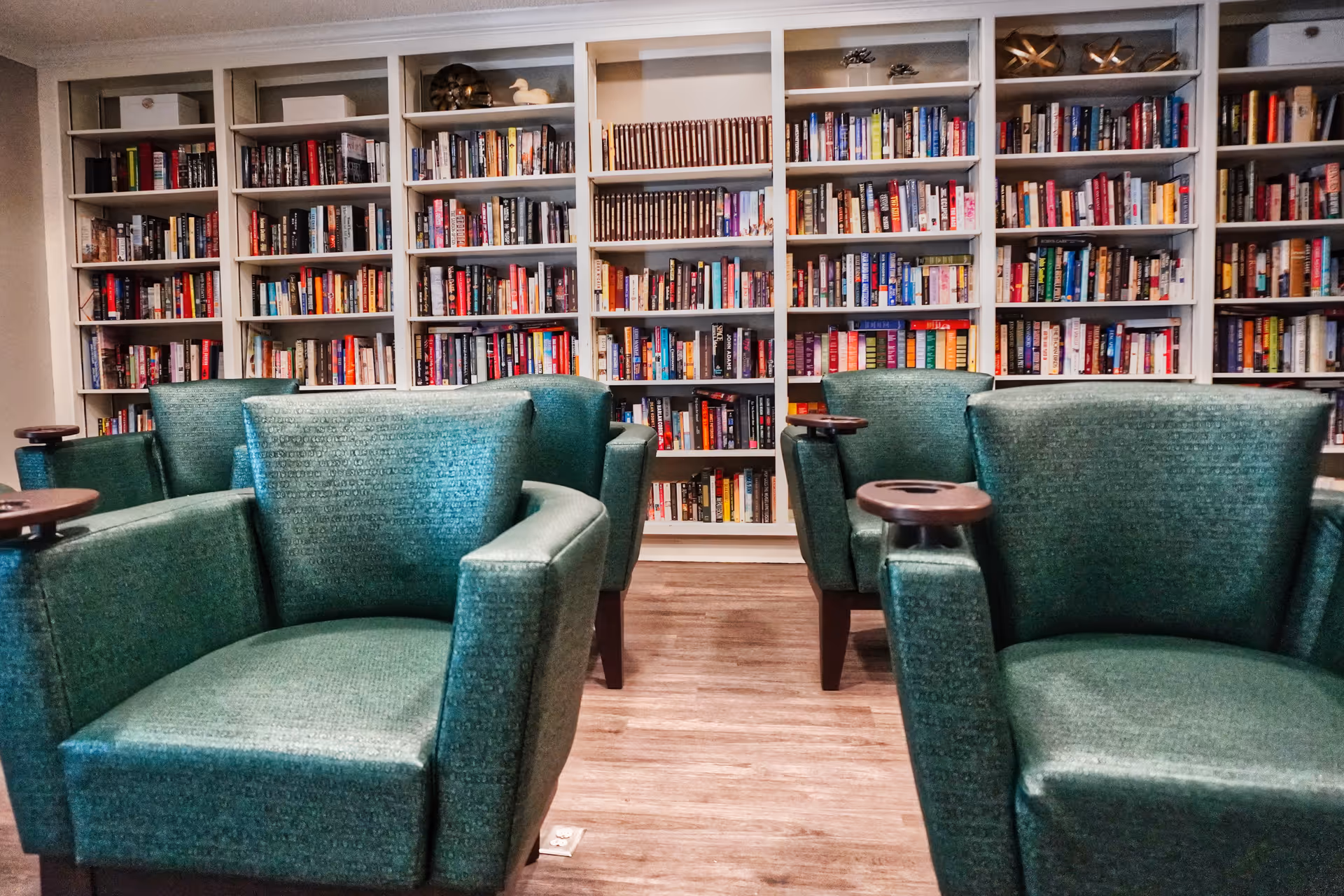 A cozy reading room with green upholstered armchairs facing tall bookshelves filled with books.