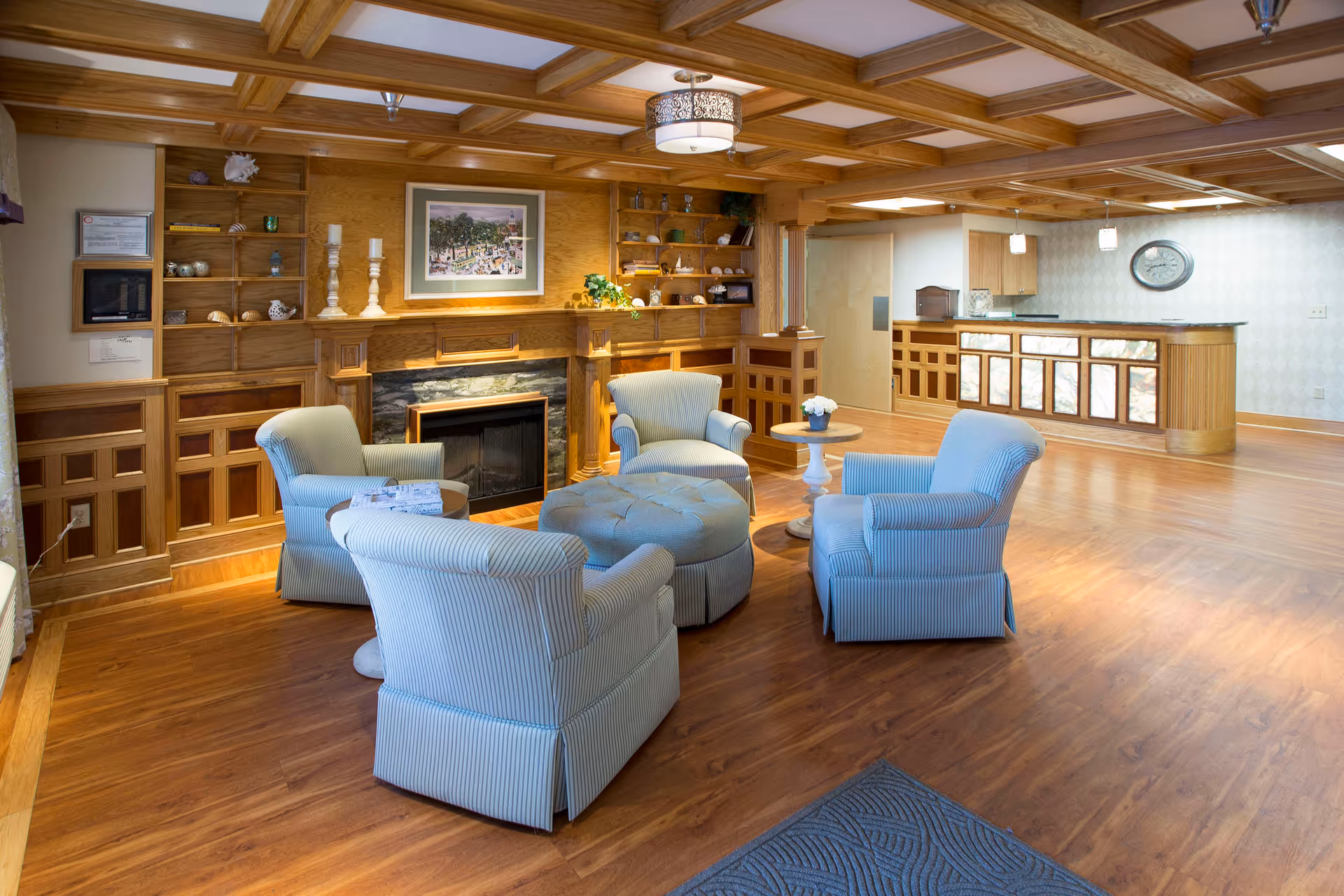 Cozy lounge with four upholstered armchairs and a round ottoman arranged around a fireplace and built-in wooden shelving, with a reception counter in the background.