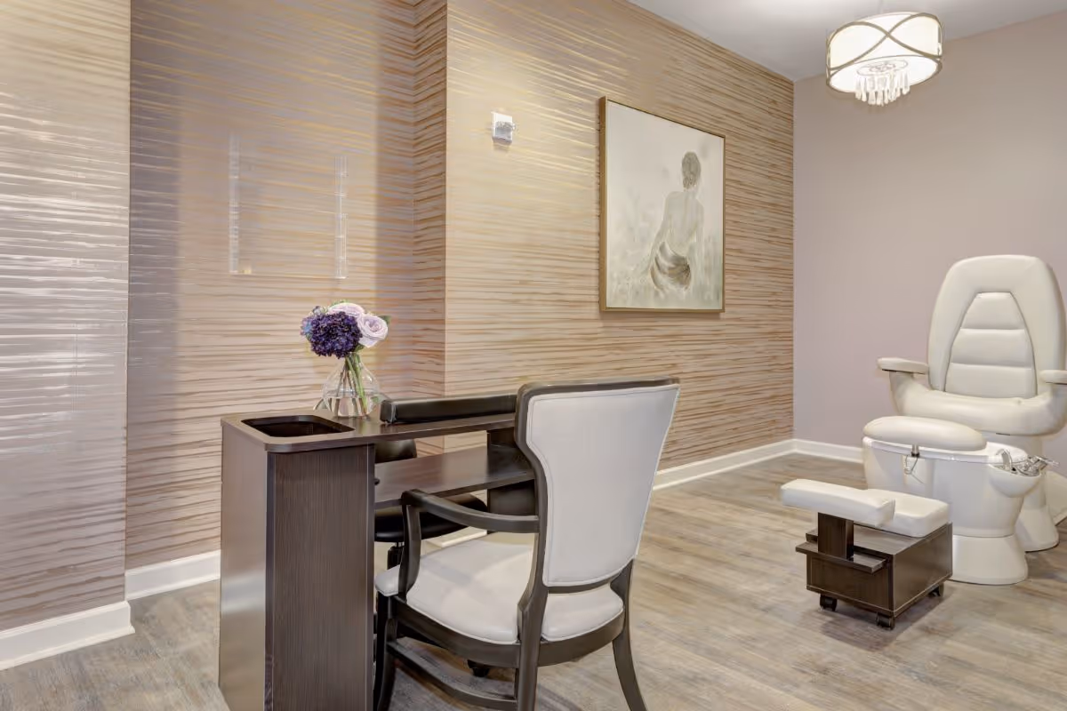 A spa-like interior with a manicure table and chair, a pedicure chair and footrest, and textured wallpaper.
