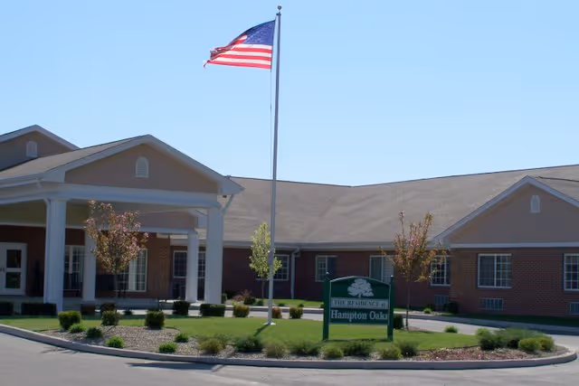 Front exterior of Hampton Oaks Health Campus building with an American flag and a sign on a landscaped circular driveway.