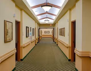 Long, well-lit hallway in Larkspur facility, with doors, art, and patterned carpet.