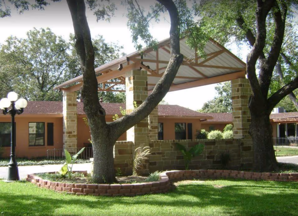 Covered stone-pillared entrance and landscaped lawn in front of a single-story nursing and rehabilitation building with trees.