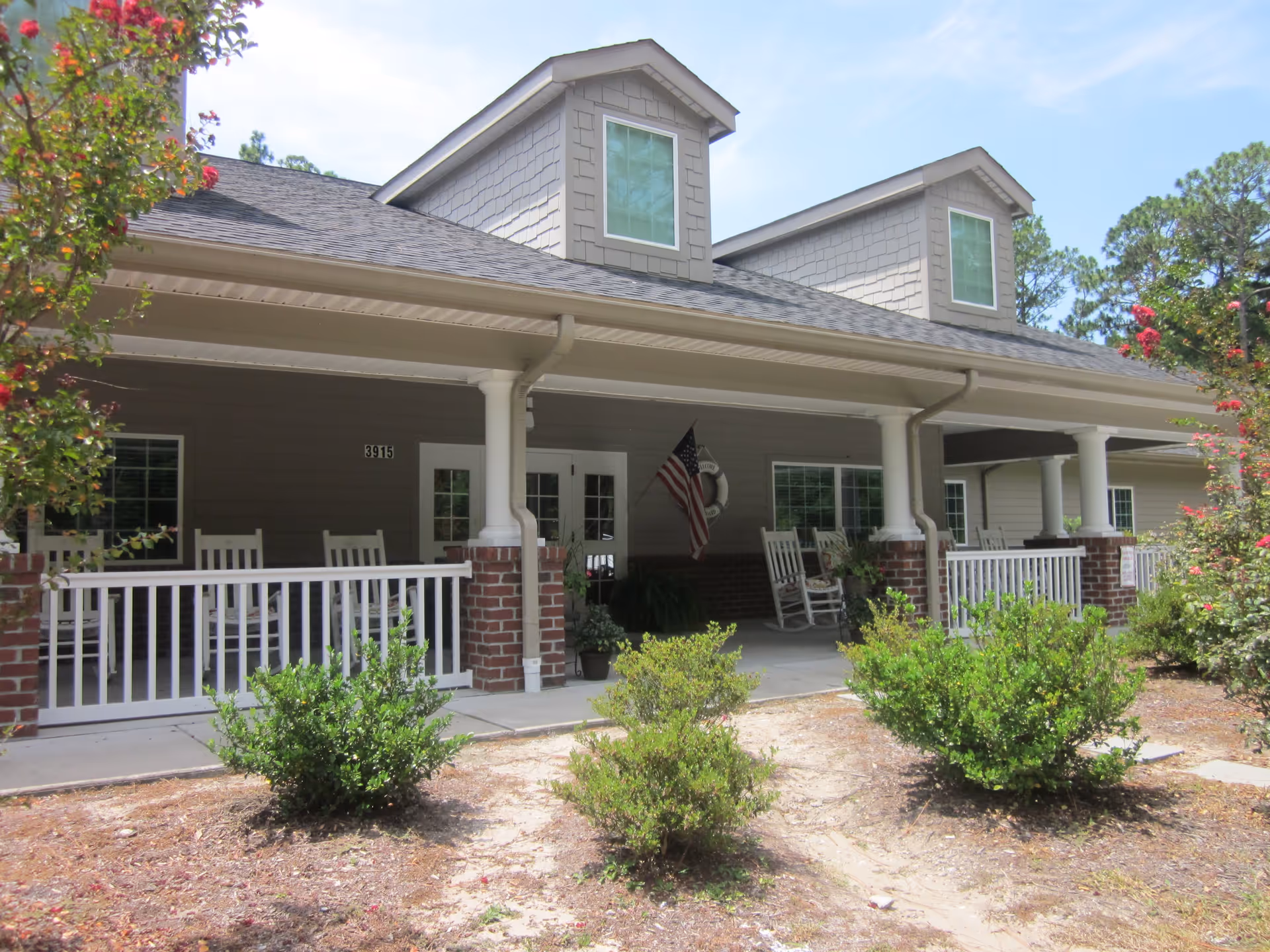 Front porch of New Hanover House with columns, white railing, rocking chairs, an American flag, and shrubs in the foreground.