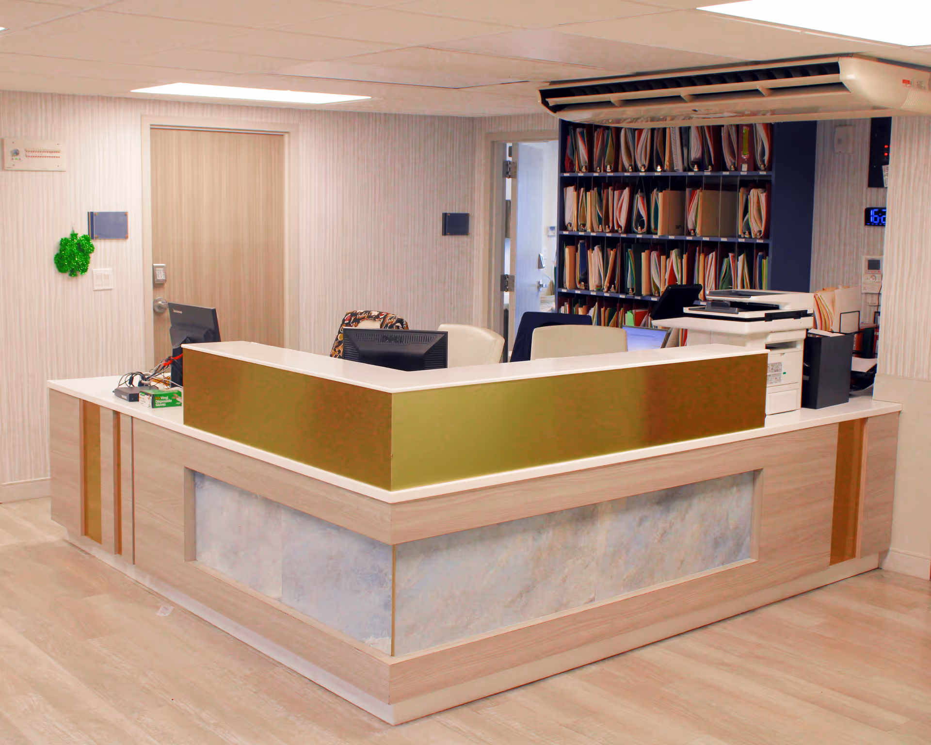 A reception desk area with computers, office chairs, a copier and shelving full of folders in a clean interior space.