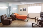 Patient room in a senior living facility with a hospital bed, recliner, nightstand, chairs and a window.