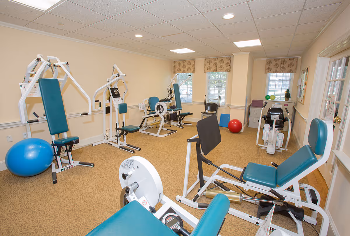 A well-lit fitness room with multiple weight machines, exercise bikes, and stability balls.