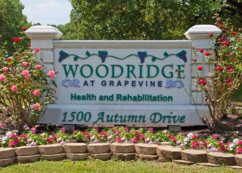 Exterior sign for Woodridge at Grapevine Health and Rehabilitation with blooming roses.