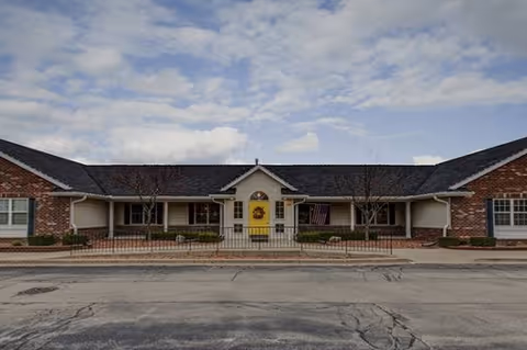 Single-story brick senior living facility with central entrance, yellow door, and benches.