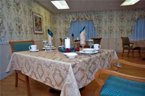 Dining room with a large table set for meals, floral wallpaper, and chairs.
