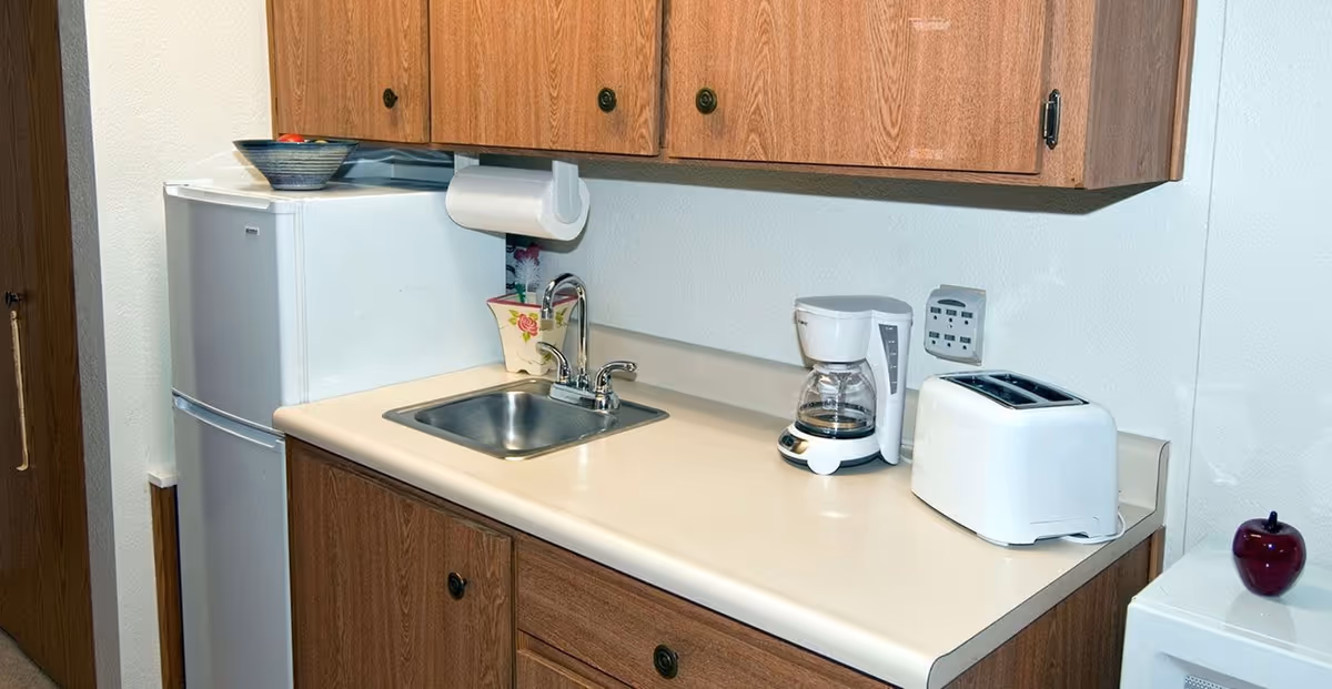 Small kitchenette with a mini refrigerator, stainless sink, coffee maker, toaster, and wood cabinets.