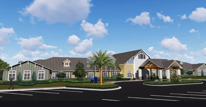 Front exterior of a single-story senior living facility with a covered porte-cochère, landscaped grounds, a palm tree, and a few people near the entrance.