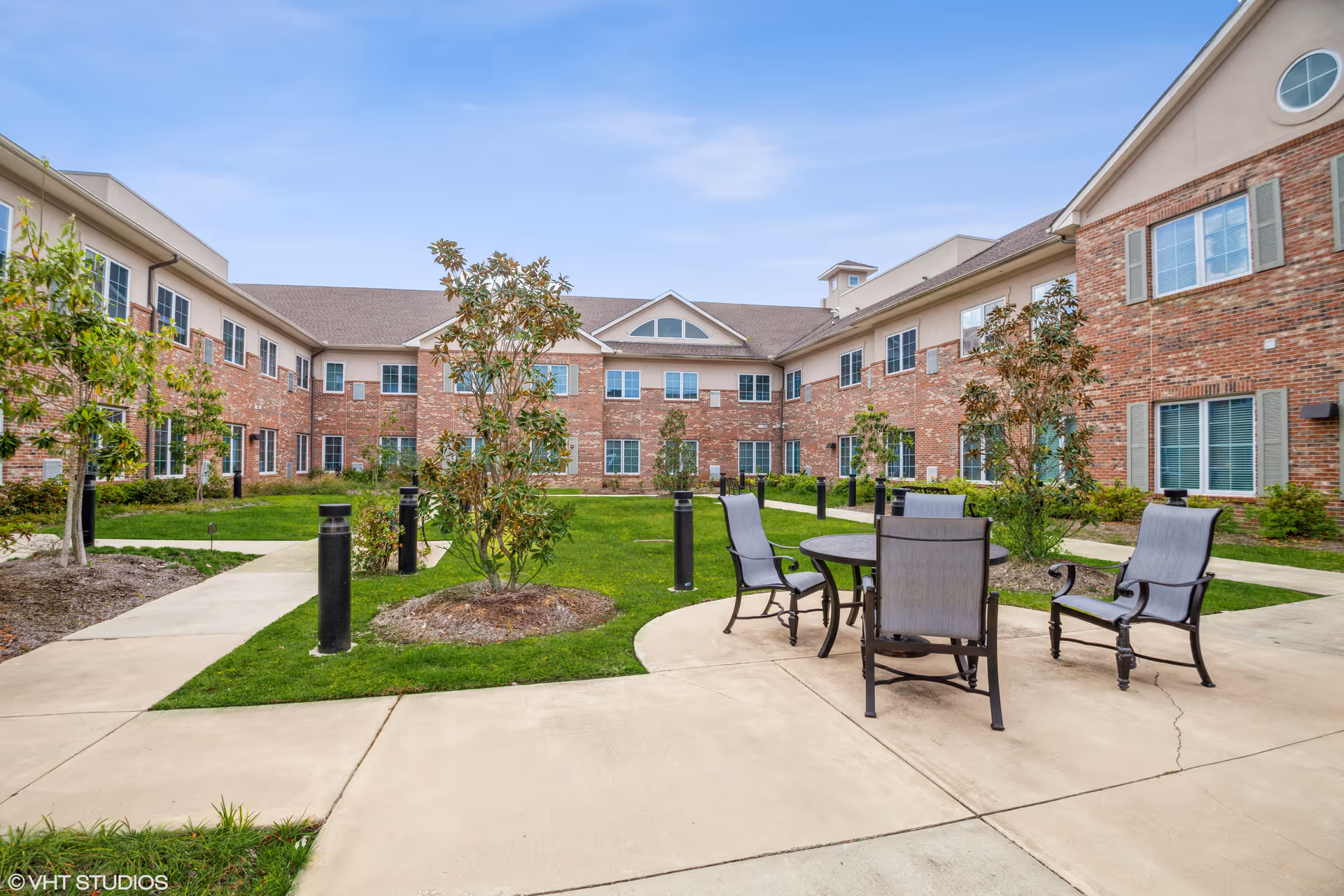 Brick senior living building surrounding a landscaped courtyard with patio chairs and a round table.