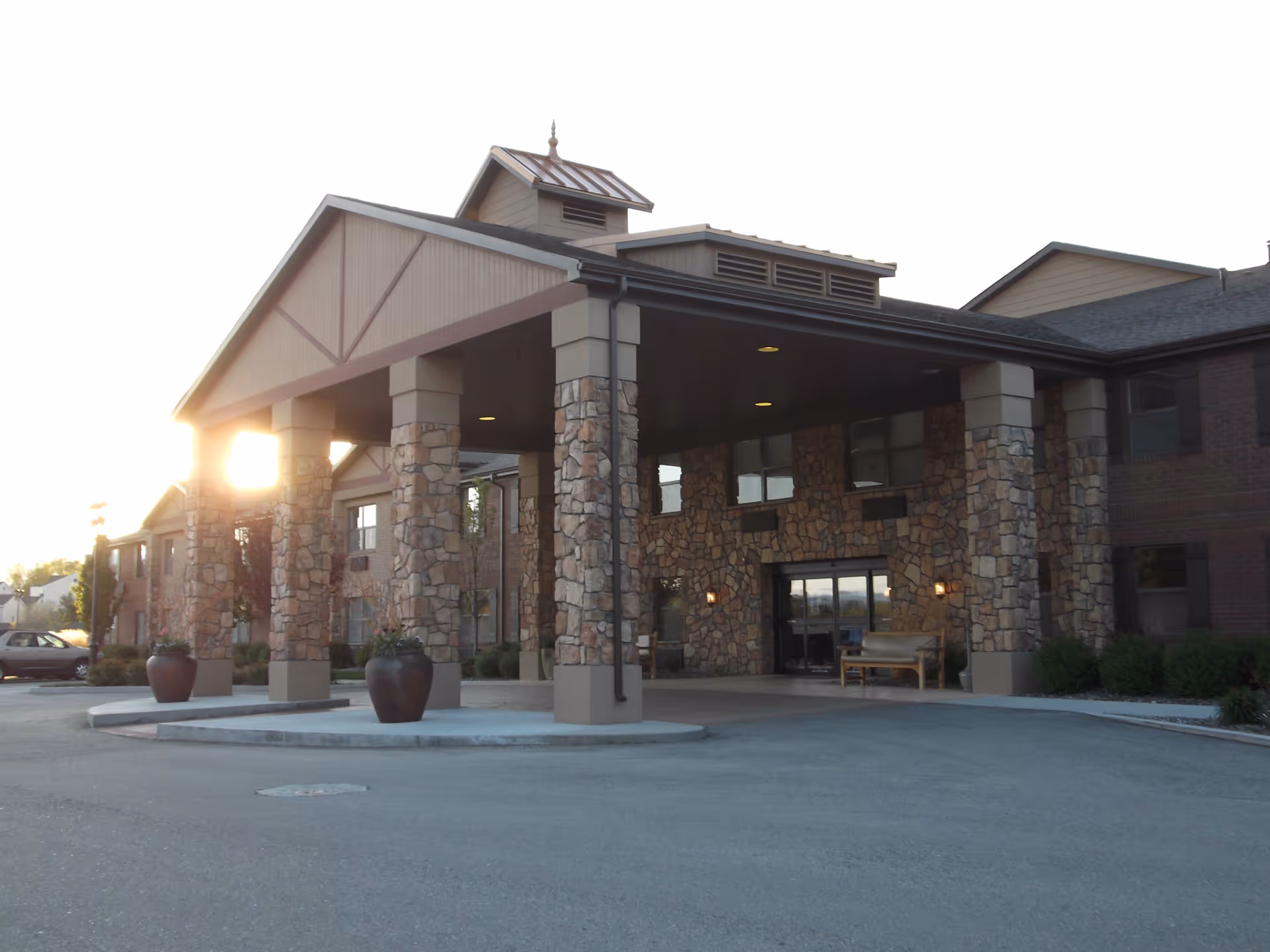 Front entrance of a stone-and-brick senior living building with a covered porte-cochère and large planters.
