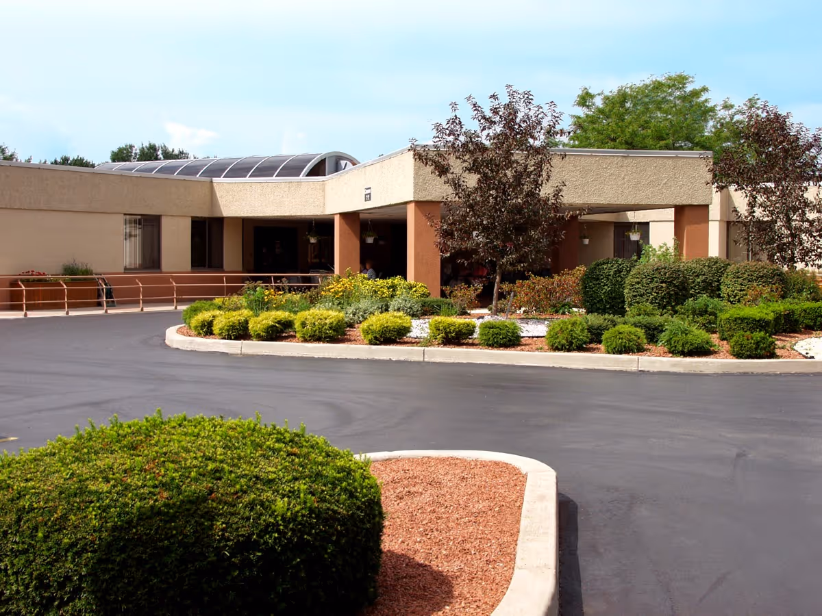 Driveway and landscaped roundabout leading to the entrance of a single-story healthcare facility with shrubs and trees.
