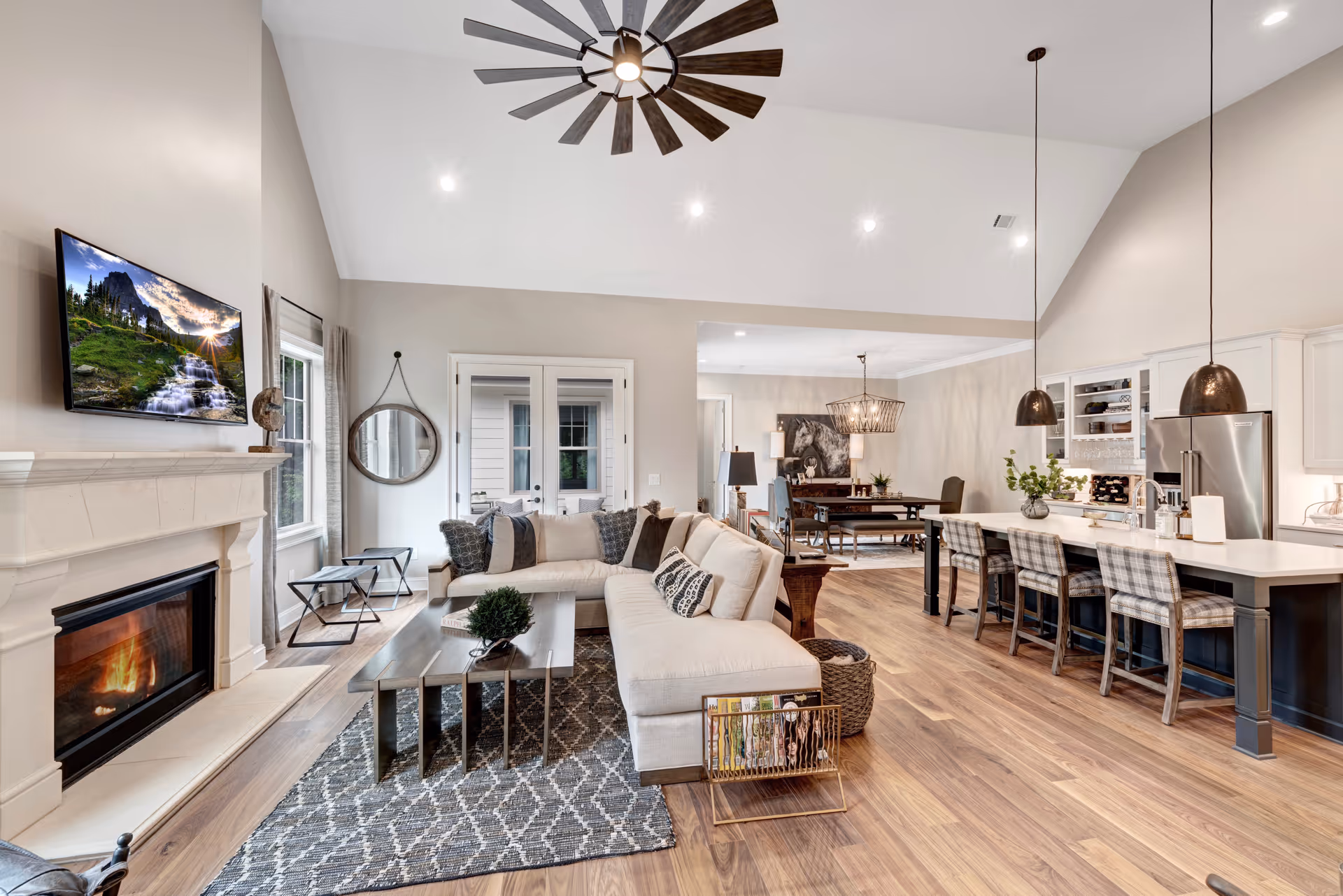 Open-concept living room and kitchen with a vaulted ceiling, sectional sofa, fireplace, coffee table, and a kitchen island with barstools.