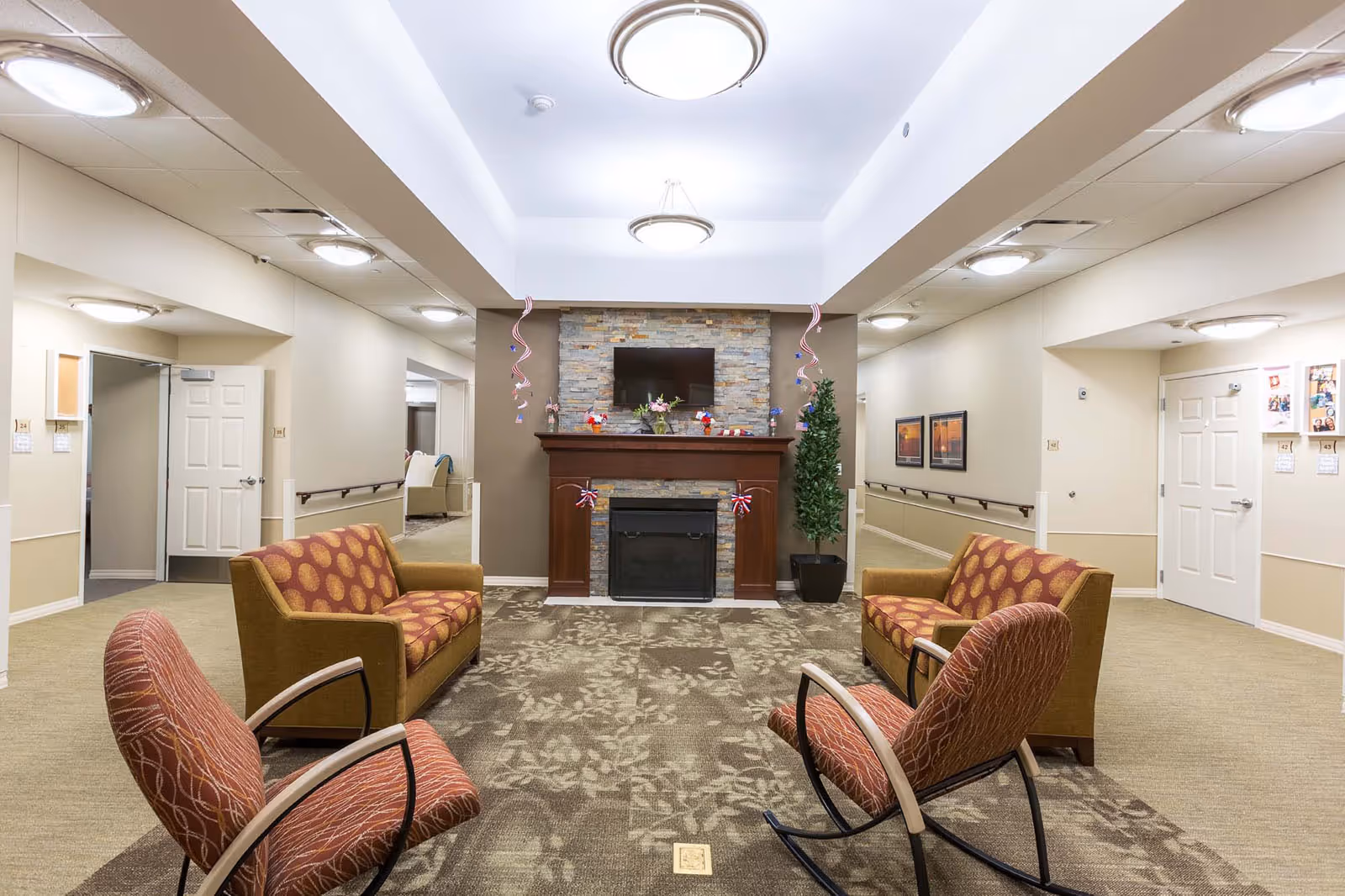 Communal lounge with sofas and chairs arranged around a fireplace and wall-mounted TV.