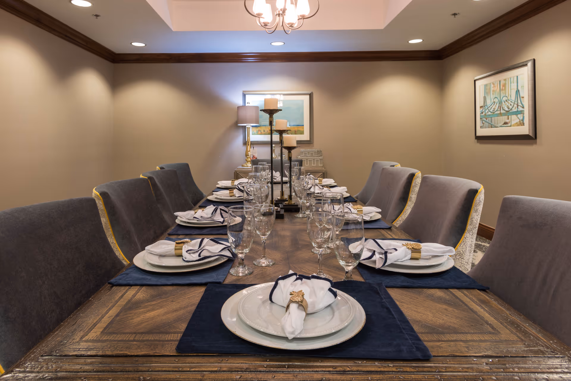 A long formal dining table set with plates, napkins, glassware and upholstered chairs in a private dining room.