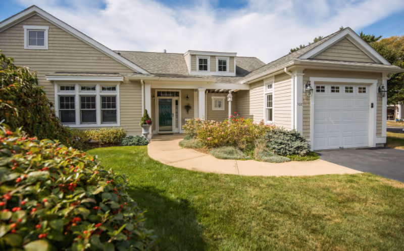 Front exterior of a single-story house with a garage, landscaped lawn and a walkway leading to a green front door.