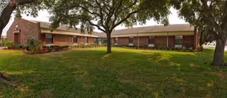 A single-story brick senior living facility with green lawn and trees in front.