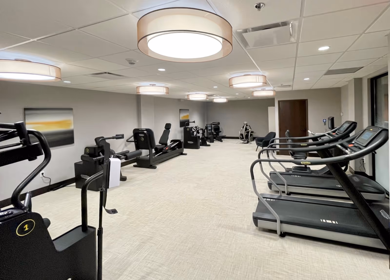 Well-lit interior fitness room with treadmills and strength machines arranged along the walls.