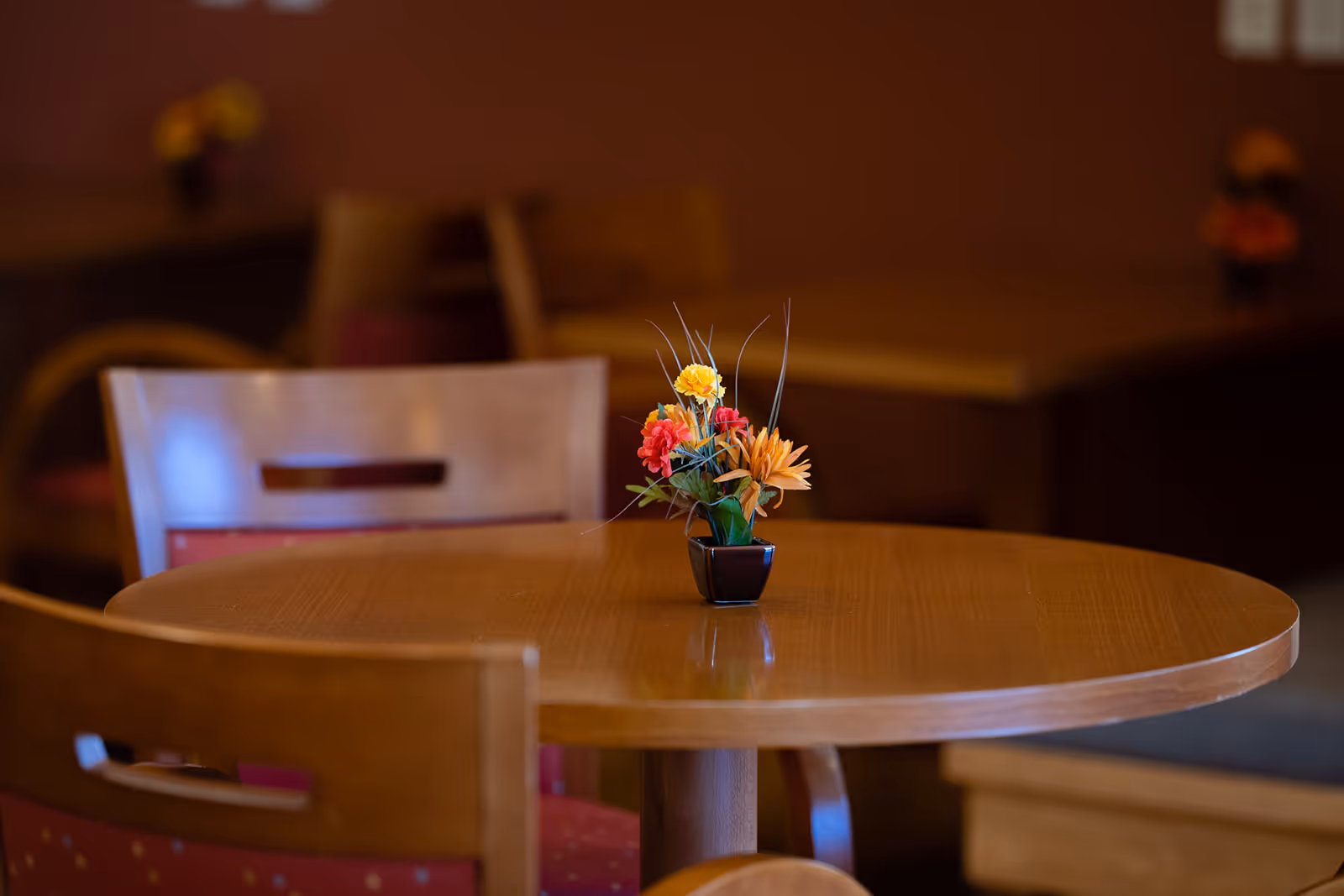 Round wooden table with a small floral centerpiece and surrounding wooden chairs in a dining area.