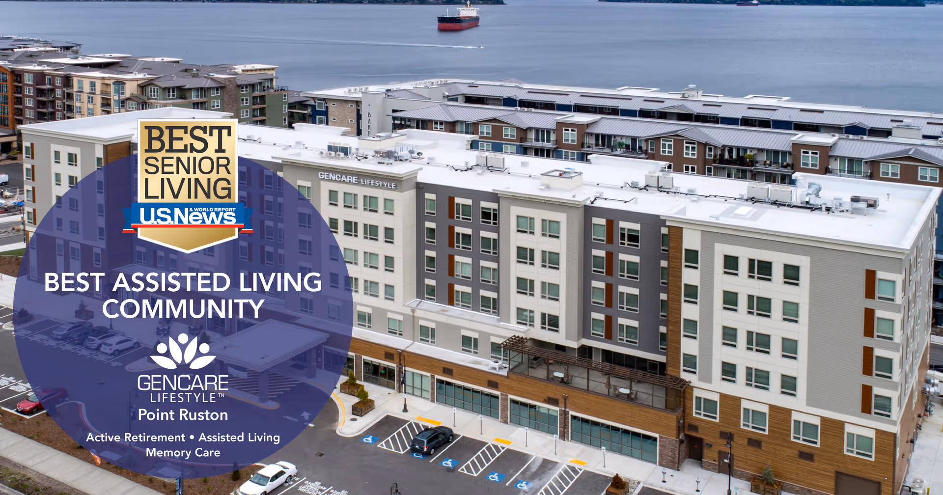 Aerial view of the GenCare Lifestyle Tacoma at Point Ruston building, a multi-story assisted living community located near a waterfront with a large ship visible in the water. The building has a modern design with multiple windows and parking spaces in front.