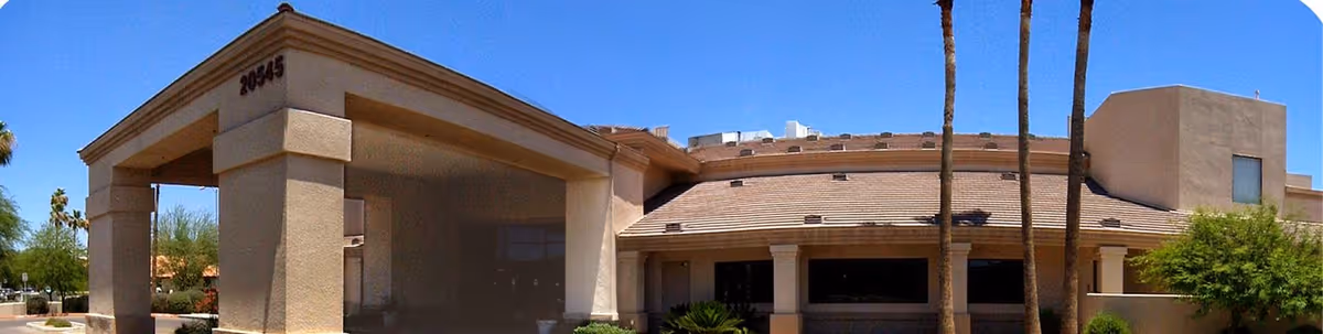 Front entrance of a beige senior living building with a covered porte-cochère and palm trees.