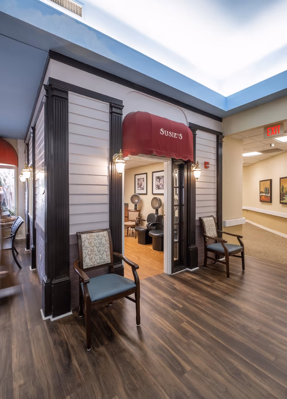 Interior hallway showing a mock storefront salon with a red awning labeled "Susie's", seating, and salon chairs inside.
