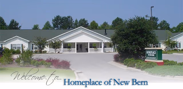 Front exterior view of Homeplace of New Bern, a single-story building with a covered entrance, surrounded by trees and landscaping under a clear blue sky.