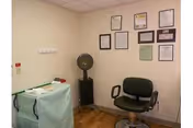 Small interior room with a salon-style chair, standing hair dryer, covered cart, and framed certificates on the wall.